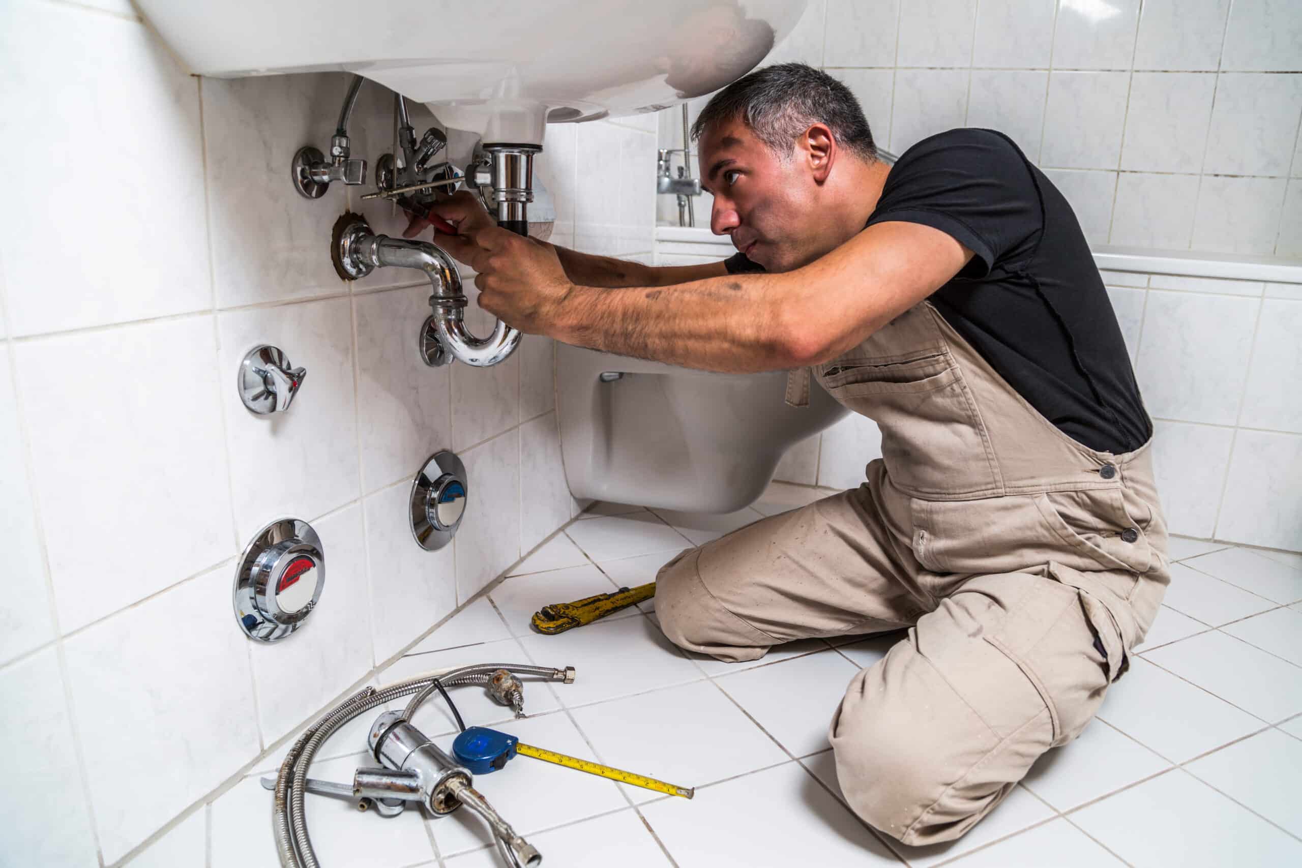 Construction worker installing plumbing under sink in bathroom